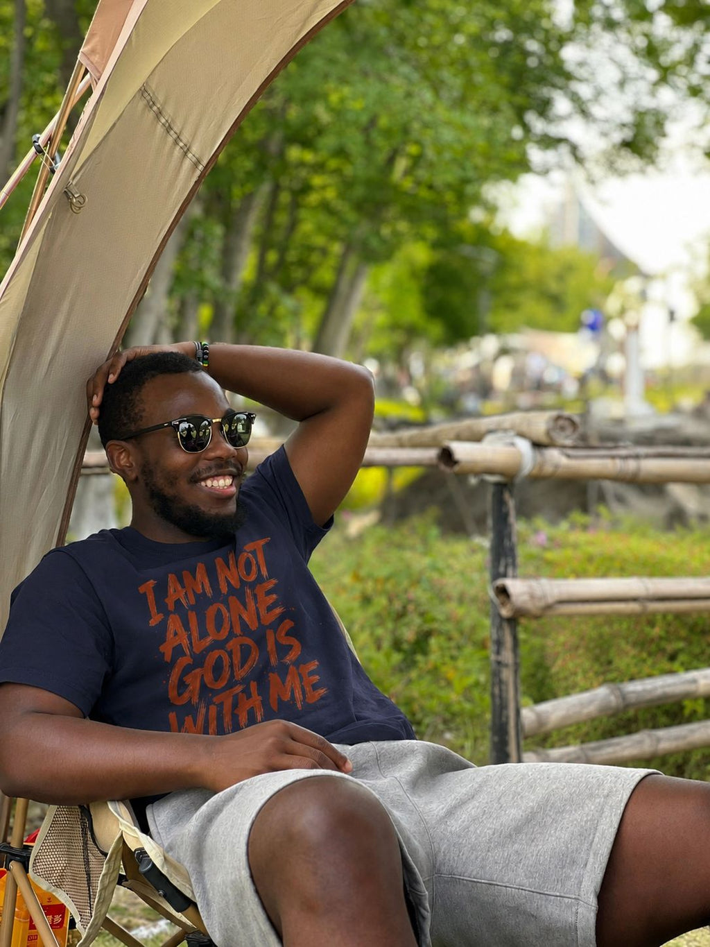Man wearing I Am Not Alone God Is With Me navy Christian faith T-shirt relaxing outdoors in a camp chair — Sister Style faith streetwear