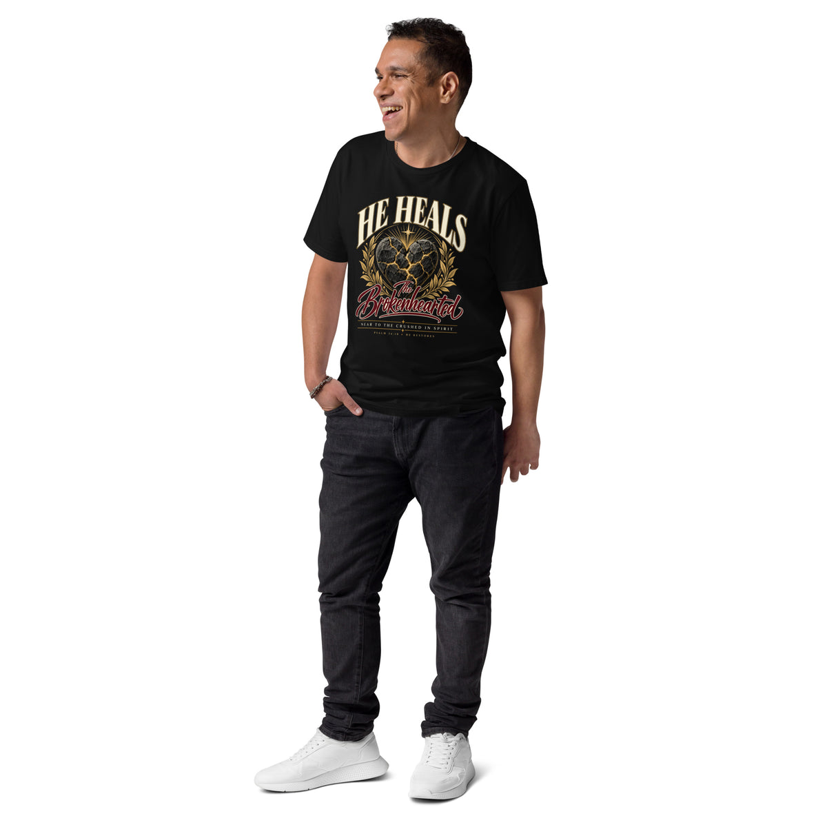 Man wearing a black He Heals the Brokenhearted organic cotton t-shirt with heart artwork, full-length view.