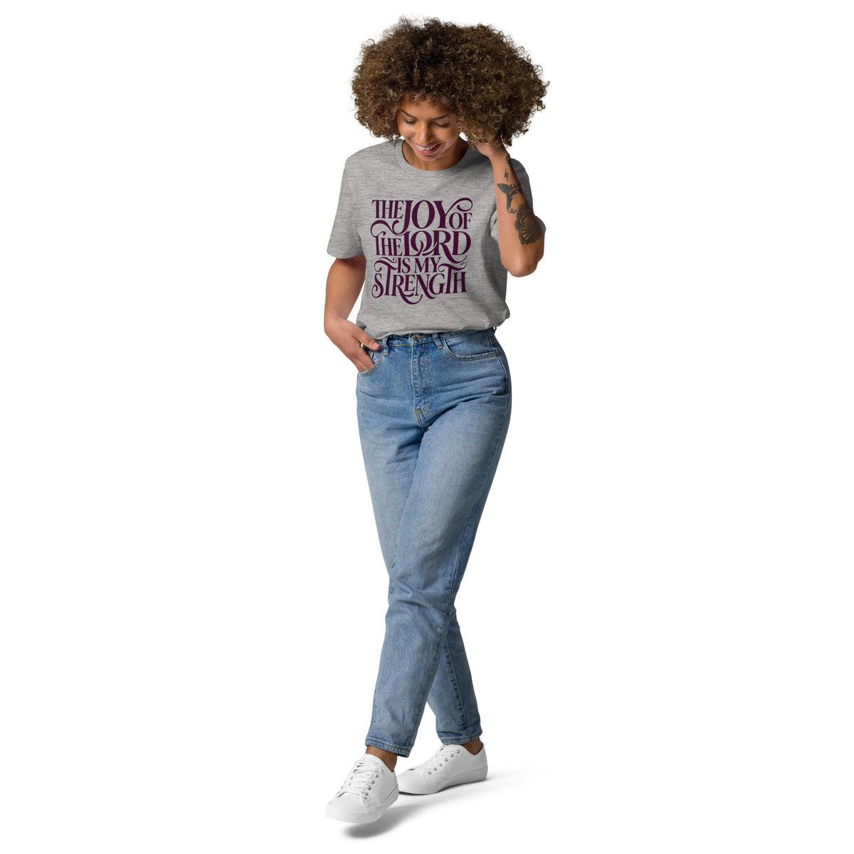Woman wearing a Heather Grey Joy of the Lord t-shirt tucked into jeans, with dark flowing faith lettering, full-length view.