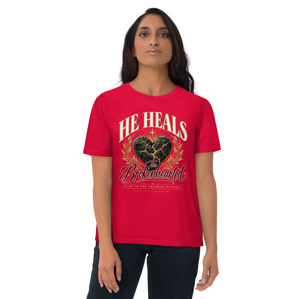 Woman wearing a red He Heals the Brokenhearted organic cotton t-shirt with a cracked heart graphic and gold-coloured branches, front view.